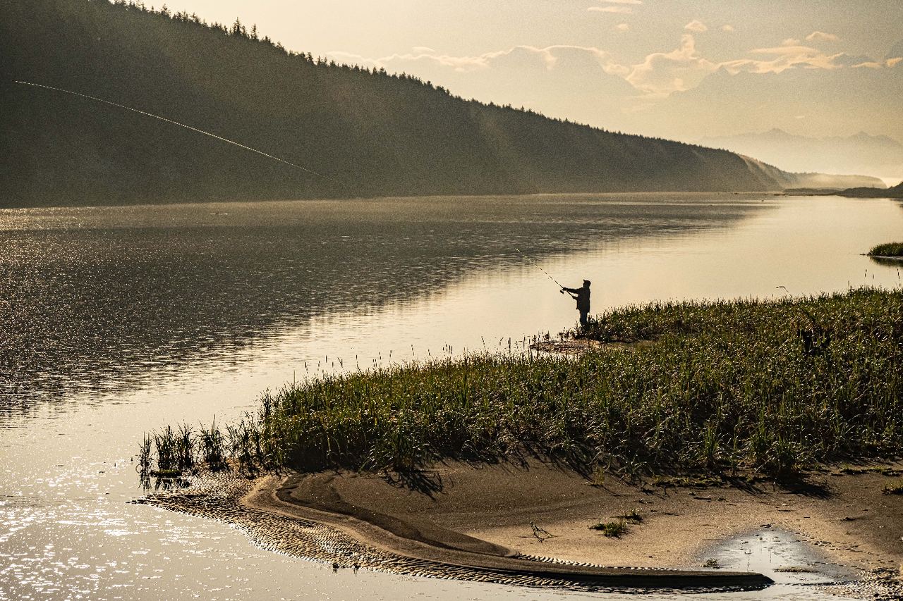A lone fly angler casting on a glassy river at golden hour.
